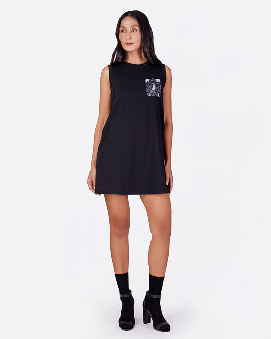 Woman wearing a black sleeveless cotton tank dress with a printed pocket design on a white background