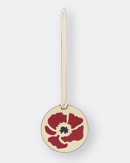 Ivory poppy bag charm hanging from a black leather bucket bag on a cafe table