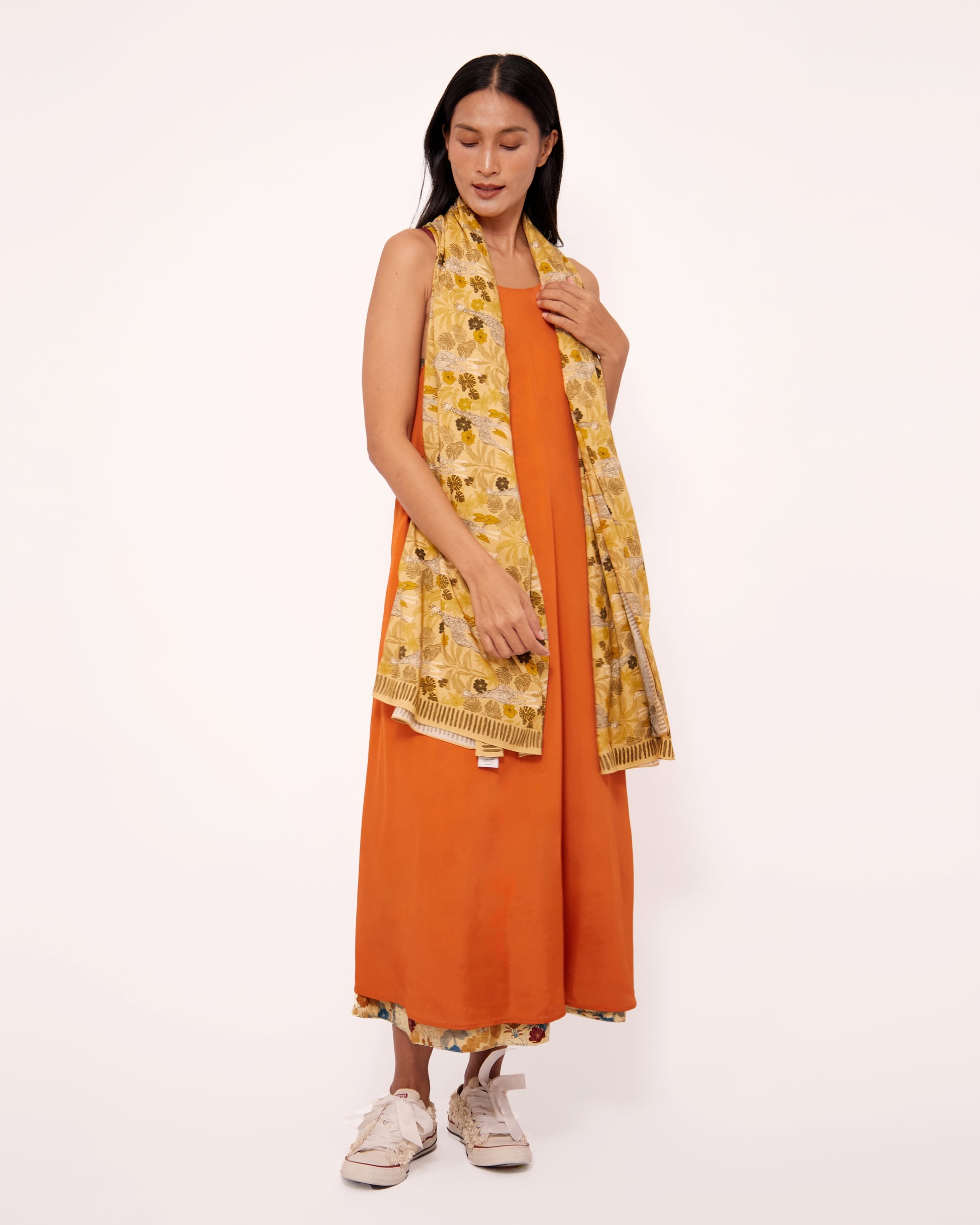 Woman wearing an orange sleeveless dress with a yellow scarf with hand drawn giraffe pattern