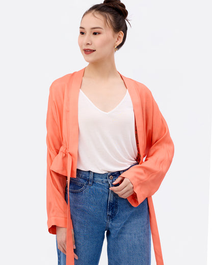 Woman wearing a coral silk blend cardigan over a white shirt and blue jeans