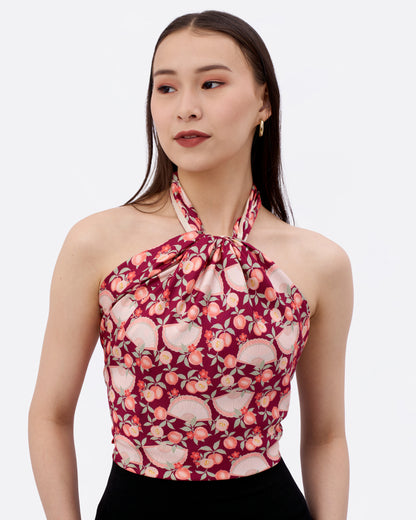 Woman wearing a reversible silk scarf in maroon colour with peaches, fan and ingot in the design as a halter top
