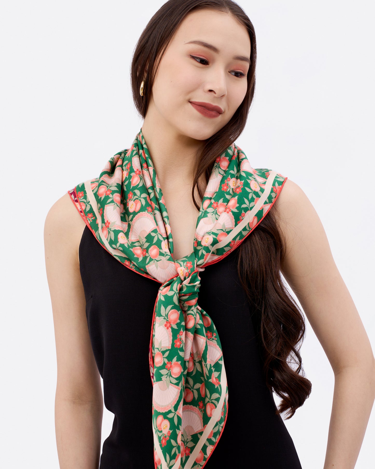 Woman wearing a emerald green patterned reversible silk scarf with peaches, fan and ingots in the design