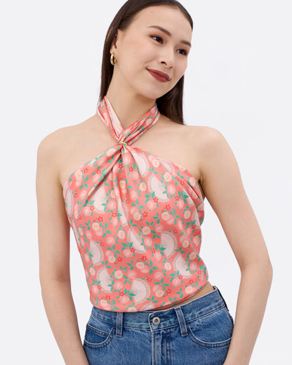 Woman wearing a reversible silk scarf in a coral colour with original prints as a halter top with a scarf ring matched with jeans