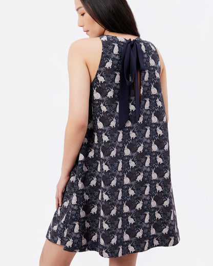 Woman wearing a black silk blend dress with hand drawn rabbit pattern and ribbon detail at the back on a white background