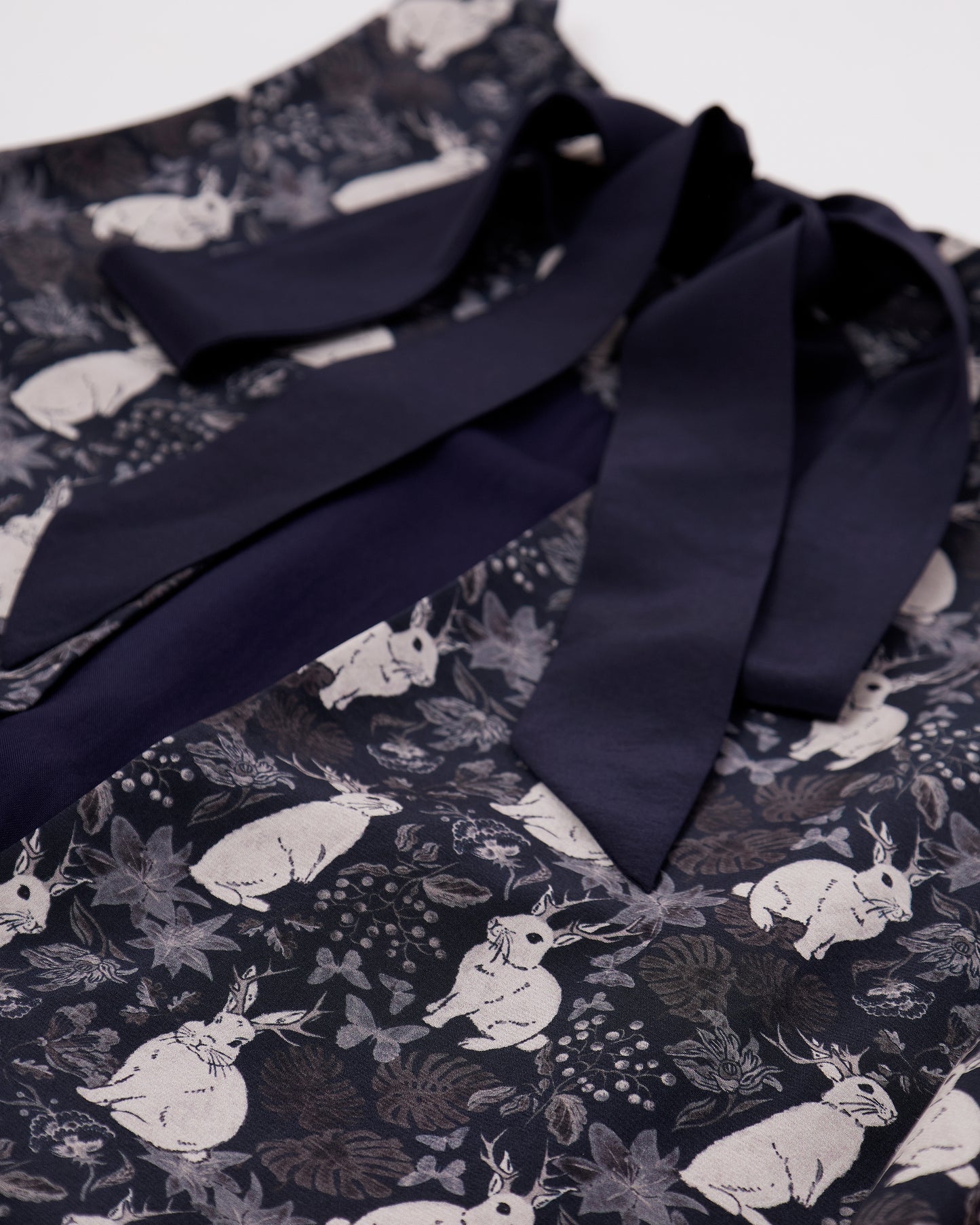 Close up of black silk blend dress with mythical rabbit pattern and back bow details with white background