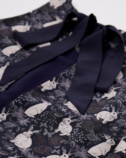 Close up of black silk blend dress with mythical rabbit pattern and back bow details with white background