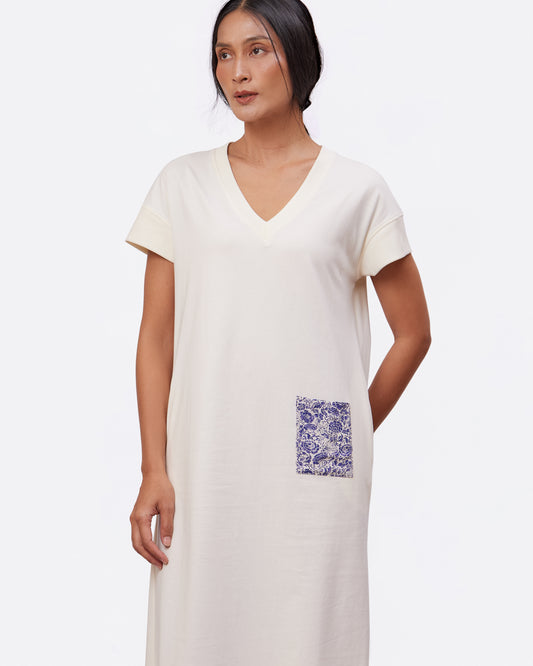 Woman wearing a white cotton maxi dress with a floral printed pocket on a plain background