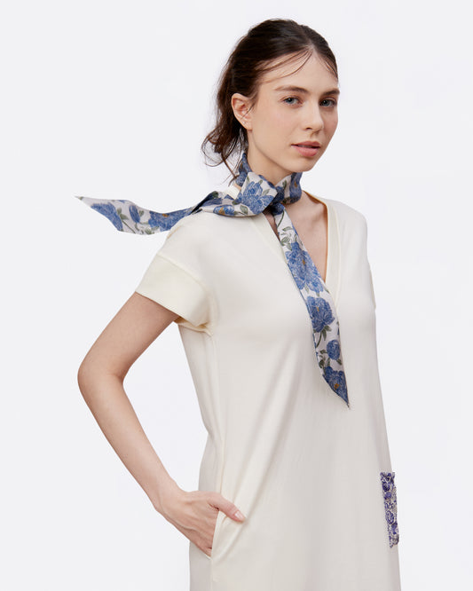 Woman wearing a white cotton maxi dress with a blue floral twilly with peony prints around her neck 