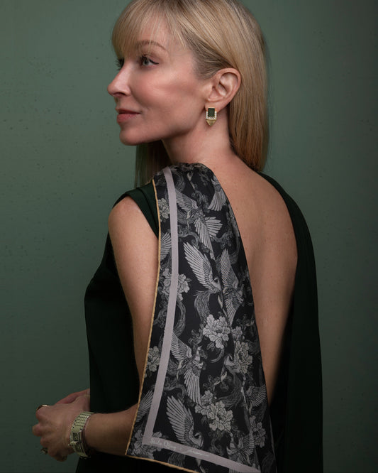 A person wearing a black dress with a double-sided silk scarf featuring a floral pattern in a dark color, with hand-rolled edges.