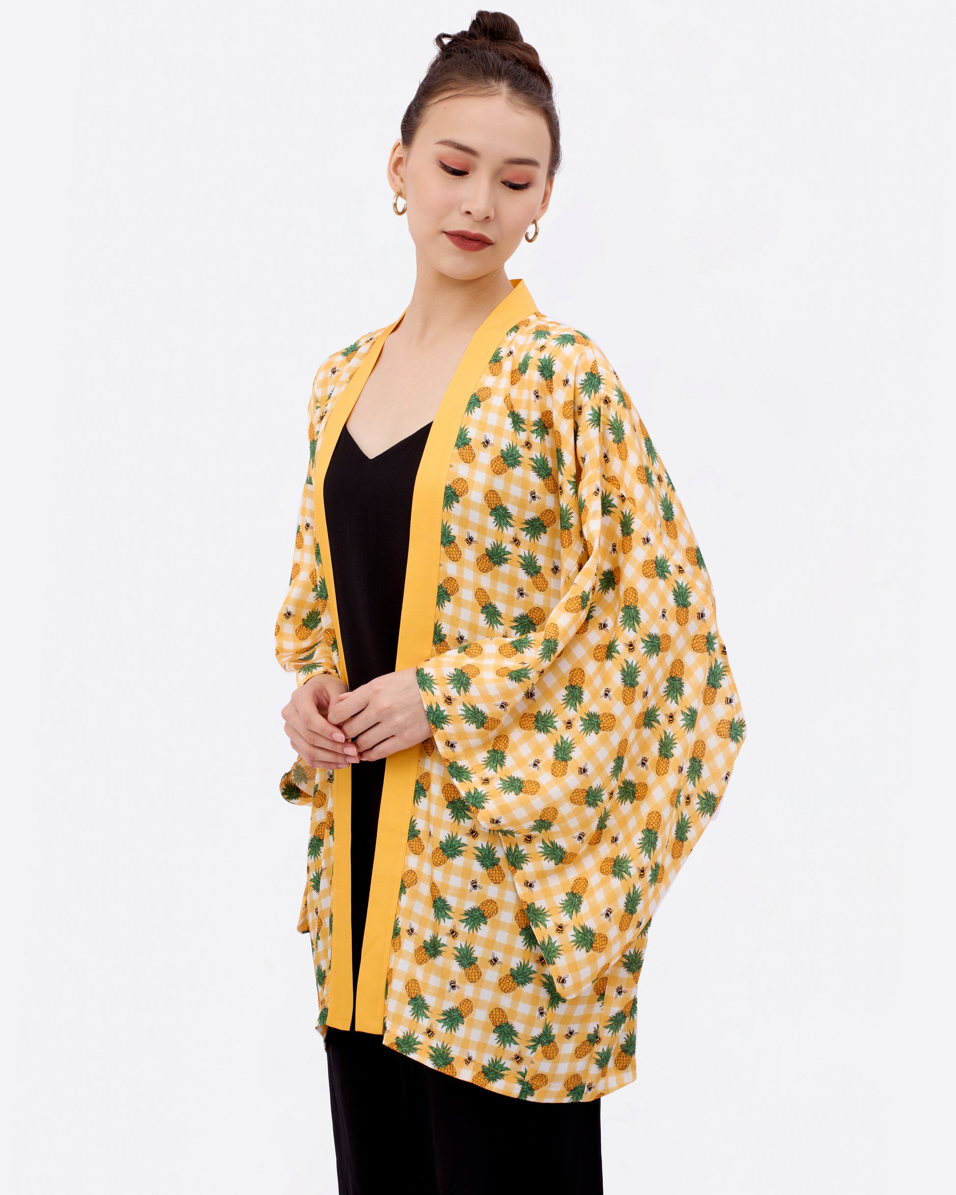 Woman wearing a yellow kimono-style jacket with pineapple, bees and checkered print