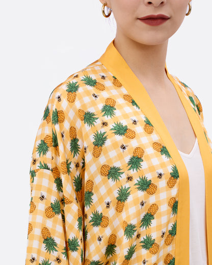 Woman wearing a yellow silk blend kimono style cardigan with hand-drawn pineapple and checkers pattern 