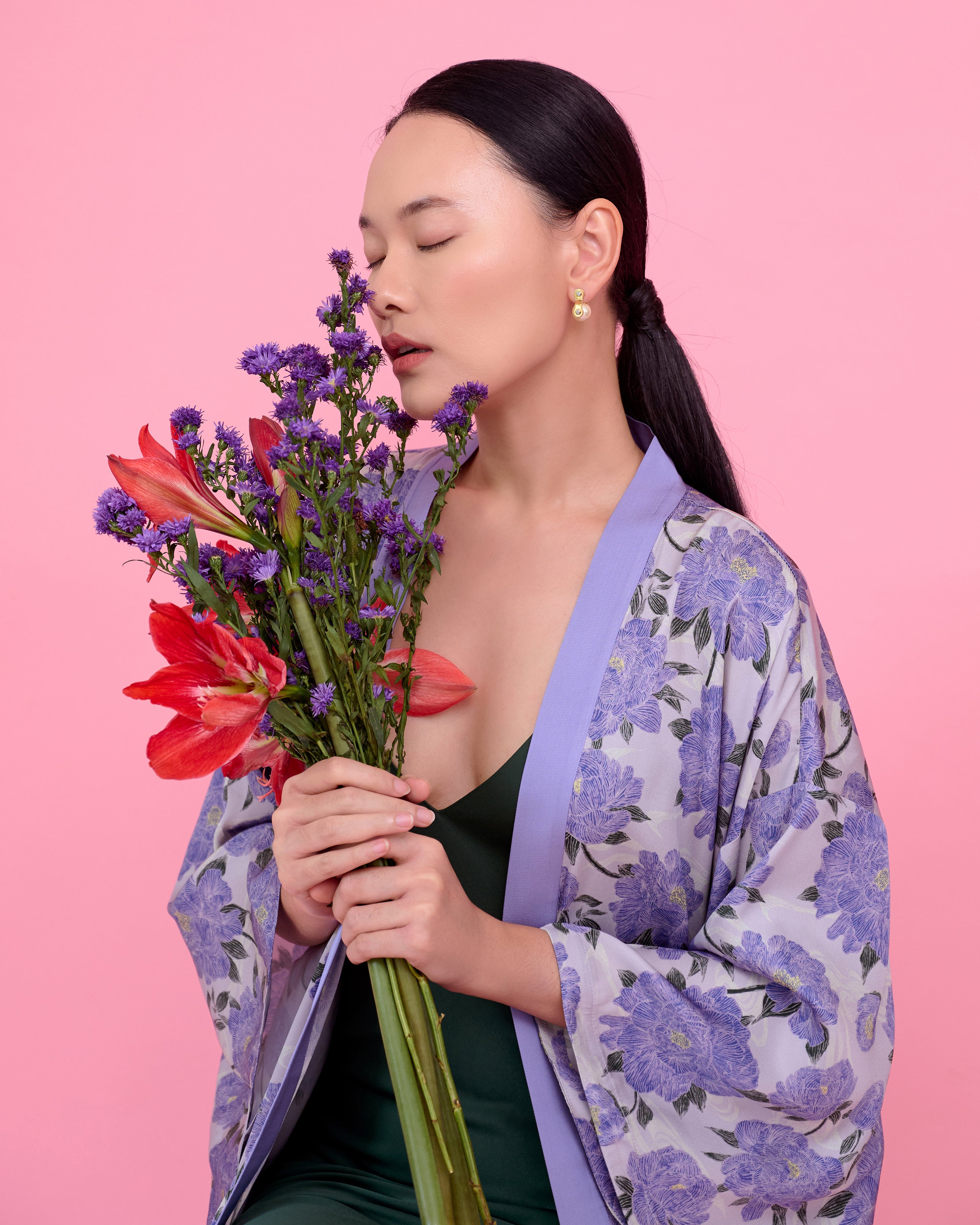 Woman holding a bouquet of flowers and wearing a silk kimono against a pink background