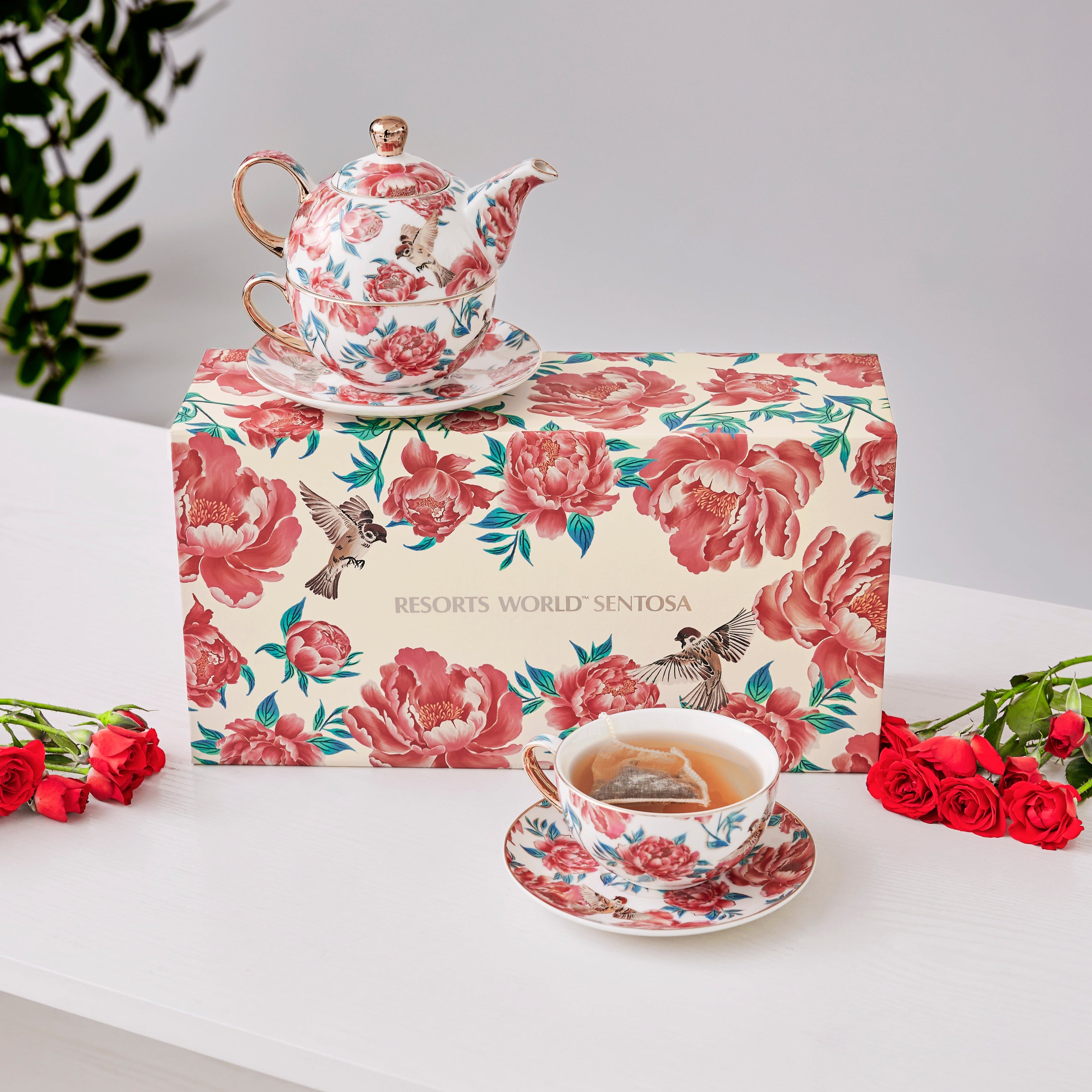 Custom tea set designed by Studio Qiling for Resorts World Sentosa (RWS) with floral design on a matching box, surrounded by red flowers on a white surface. For mid-autumn festival gifting