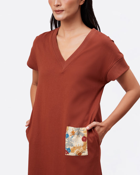 Woman wearing a rust-colored v neck cotton maxi dress with a safari elephant print pocket detail